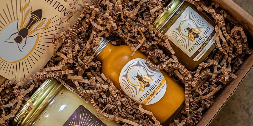 Three jars of honey in a box with bee-themed labels on a textured surface.