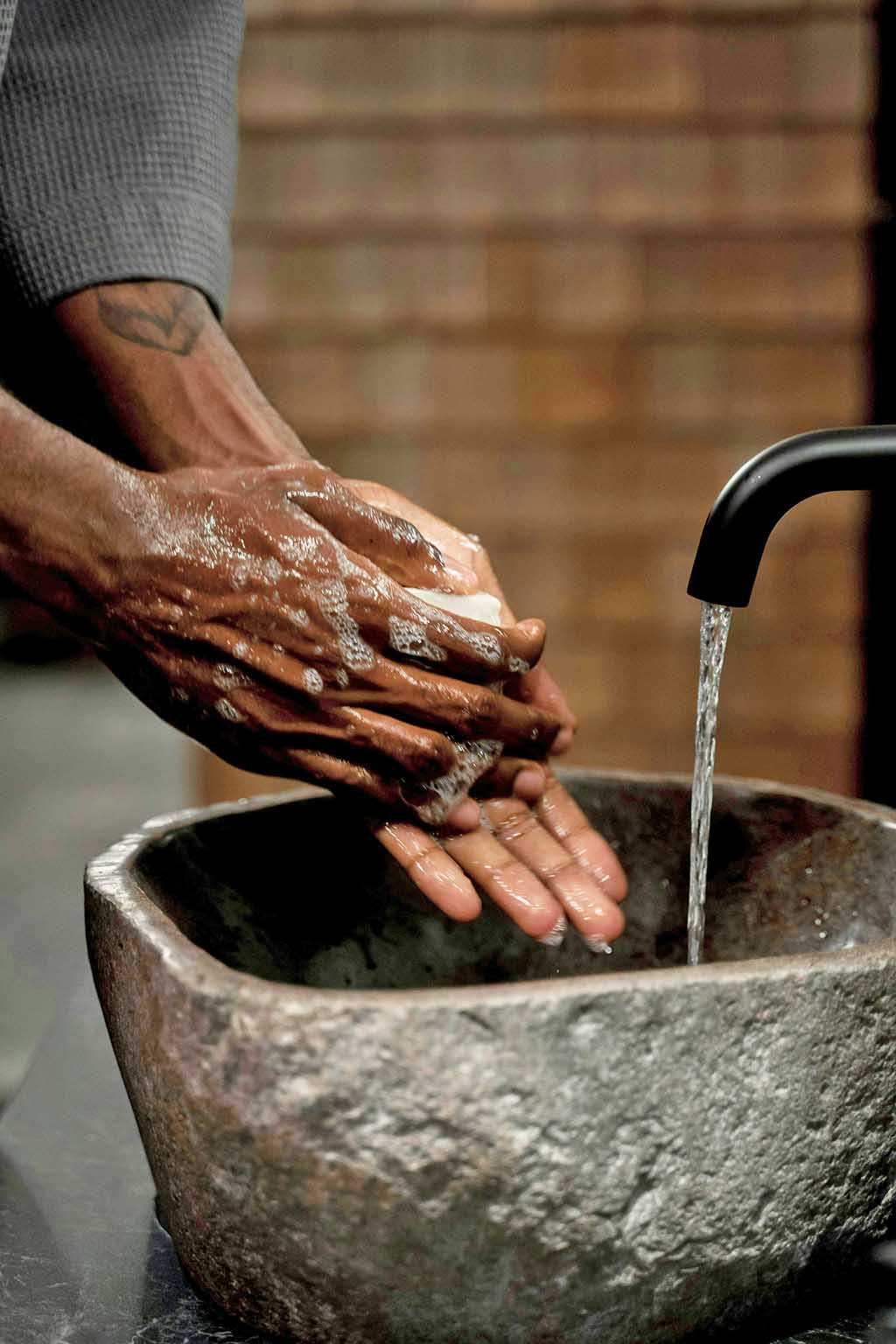 Person washing hands with soap under running water from a black faucet over a stone basin.
