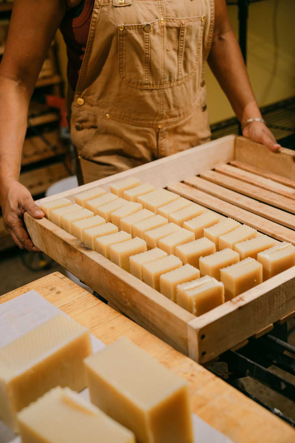 Person holding a wooden tray of soap bars in a workshop setting